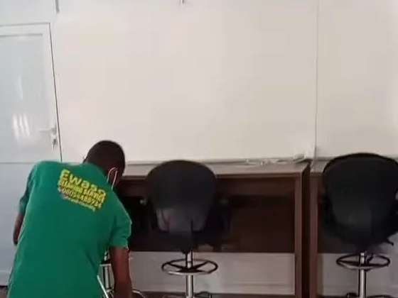 An Ewaso cleaner in a green uniform mopping an office floor beside desks and office chairs
