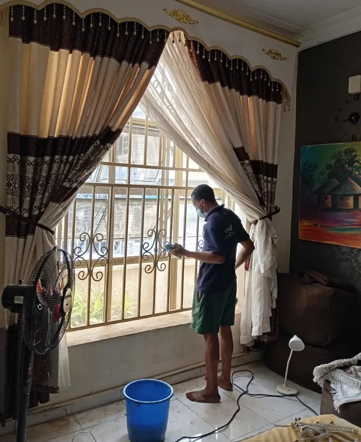 An Ewaso cleaner washing a living-room window between patterned curtains